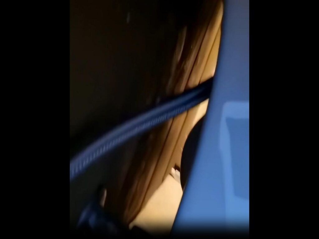 暗い隙間に青いホースのような物がある