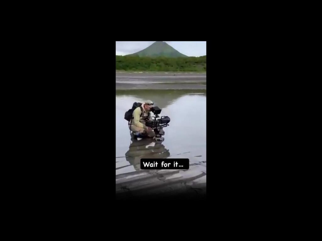 水辺でカメラを構えて座る撮影者と山